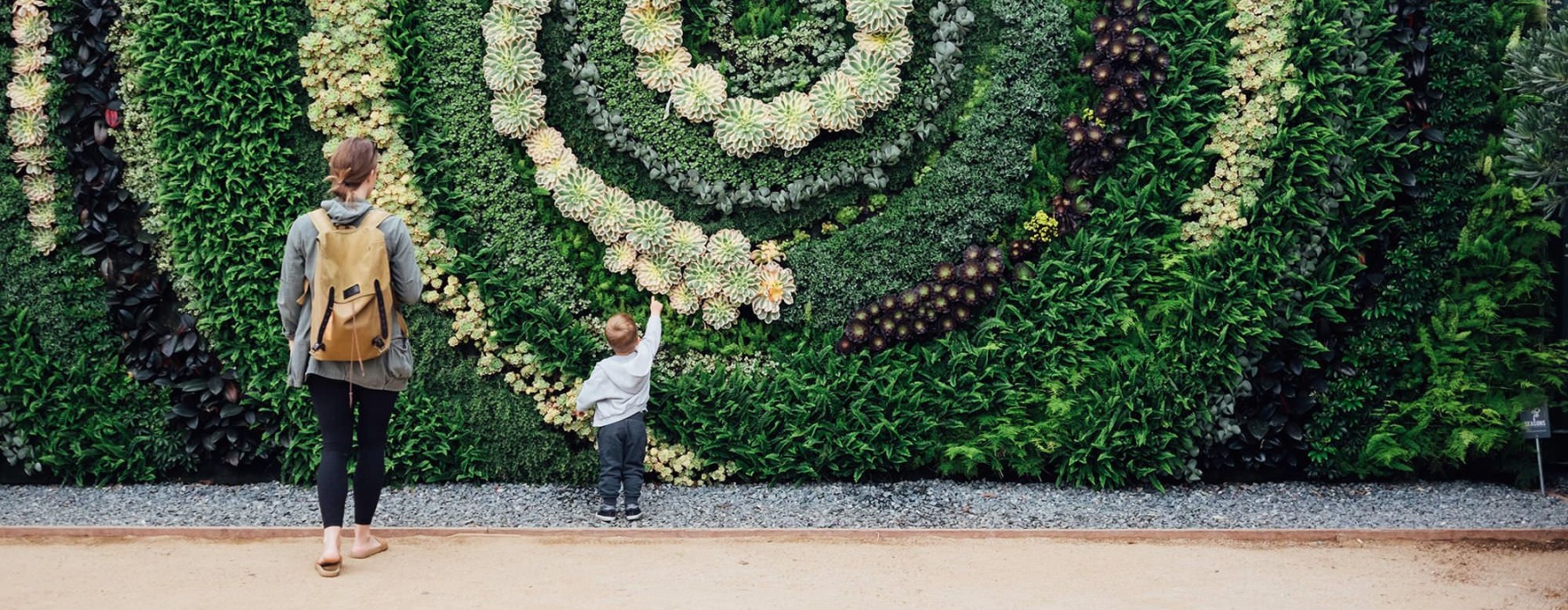 mother and child standing in front of a mural made of plants